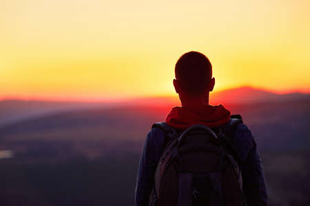 Traveler with backpack watching amazing sunset. Silhouette of the young man on the mountain top. Krkonose mountains, Czech Republicの写真素材
