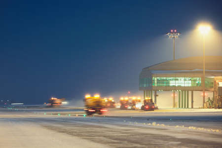 Airport during the snowstorm. Snow plows cleared the snow from the runways and taxiways. - selective focus on terminal buildingのeditorial素材