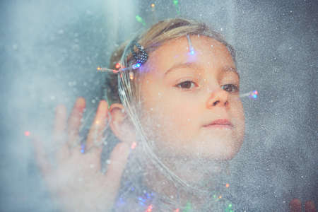 Christmas surprise is coming. Little girl looking through the icy and snowy window. - Dreamy style and selective focusの写真素材