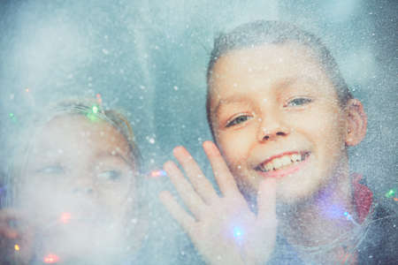 Christmas surprise is coming. Little girl a little boy looking through the icy and snowy window. - Dreamy style and selective focusの写真素材