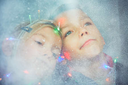 Christmas surprise is coming. Little girl a little boy looking through the icy and snowy window. - Dreamy style and selective focusの写真素材