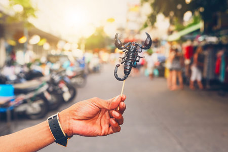 Hand of the Thai vendor showing roasted scorpio. Street market in central Bangkok, Thailand.