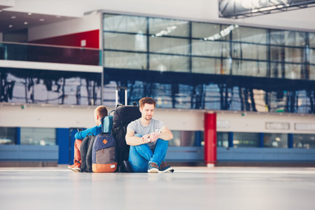 Two friends traveling together. Travelers with mobile phones waiting at the airport departure area for their delay flight.の写真素材