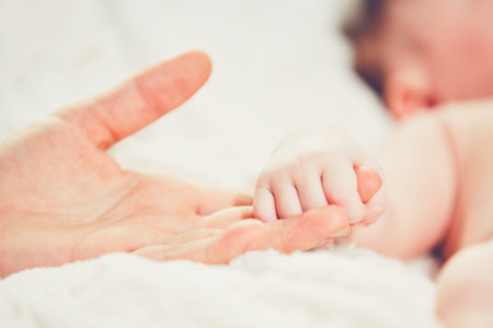 Touch of the motherhood. Hand of mother and her baby in the bed. Son holding his moteher.