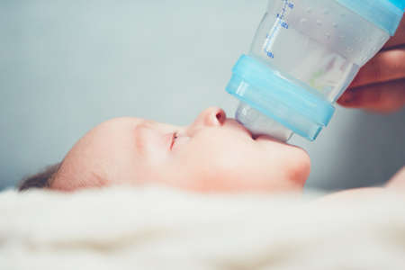 Hungry baby drinking milk. Mother feeding her little boy from bottle.の写真素材