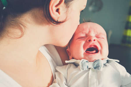 Mother holding crying baby. Young woman with her little son. の写真素材