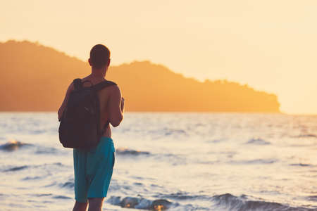 Young traveler with backpack watching amazing sunset. Vacation on the tropical beach.の写真素材