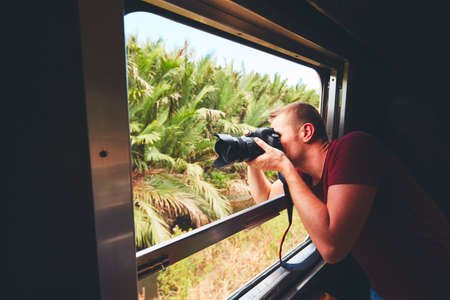 Young traveler on the holiday. Photographer with dslr camera photoshooting from open window of the vintage train.の写真素材