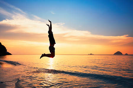 Joyful young man jumping into the sea during beautiful sunset.の写真素材