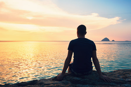 Contemplation at the beautiful sunset. Silhouette of the young man on the beach.の写真素材