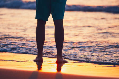 Vacations on the idyllic beach. Legs of the young man during amazing sunset.の写真素材