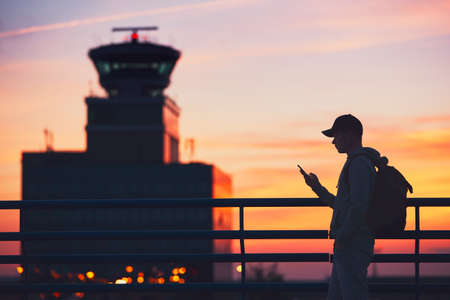 Silhouette of the traveler with mobile phone at the airport. Air Traffic Control Tower at the amazing sunset. Prague, Czech Republic.の写真素材