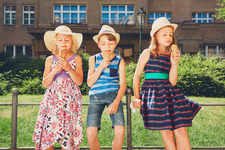 Summer day in the city. Cute siblings with hats eating big ice cream in the park.の写真素材