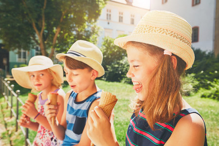 Summer day in the city. Cute siblings with hats eating big ice cream in the park.の写真素材