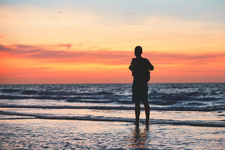 Contemplation on the tropical beach. Pensive man (tourist) standing in water of the sea during beautiful sunset.の写真素材