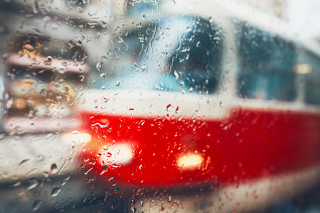 Gloomy day in the city. Tram on the street in rain. Selective focus on the raindrops on the window....