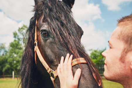 Summer day on the farm. Young man caress horse.の写真素材