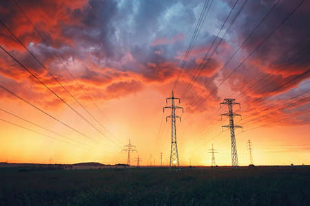 Dangerous weather. Electricity pylons with power lines in stunning storm during colorful sunset.の写真素材