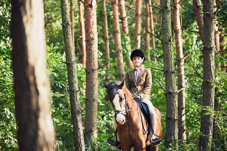 Teenage girl in formal wear riding a horse in forest.の写真素材