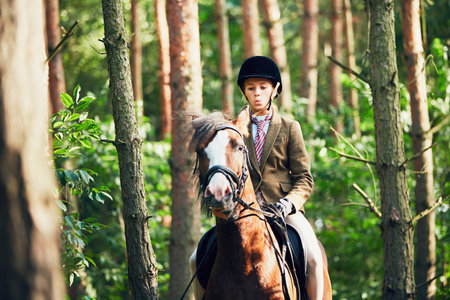 Teenage girl in formal wear riding a horse in forest.