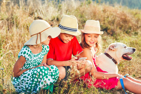 Happy children playing with smart phone. Themes friendship, summertine and modern technology