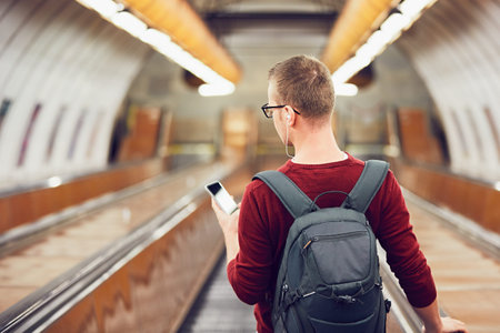 Traveling by public transportation. Young man listening music in headphones on the escalator to the subway. の写真素材