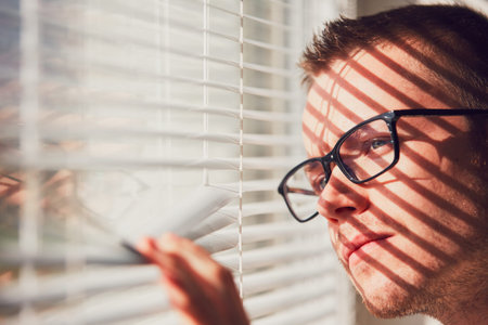 Curious man with eyeglasses looking through a jalousie. Themes curiousity, surveillance or eyesight. の写真素材
