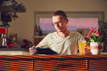 Morning time at home. Young man reading on the digital tablet in the kitchen during breakfast.の写真素材