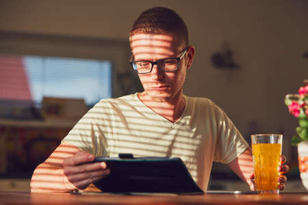 Morning time at home. Young man reading on the digital tablet in the kitchen during breakfast.の写真素材