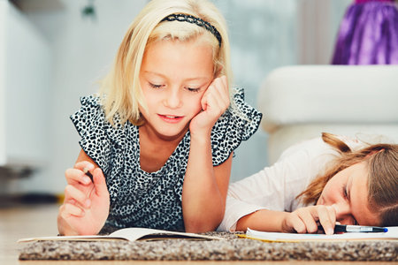 Girls lying on the carpet making their homework in elementary school.
