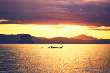Amazing sunrise on the sea. Silhouette of a small fishing boat against tropical islands between Phuket and Krabi in Thailandの写真素材