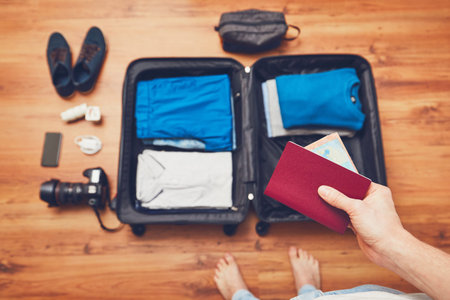 Preparing luggage for the trip. Young man packing vacation items: clothes, mobile phone, camera and...
