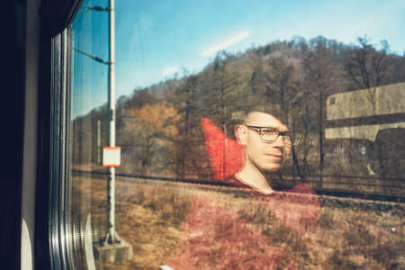 Rail transportation in sunny day. Pensive young man traveling seen though train window with reflection. の写真素材