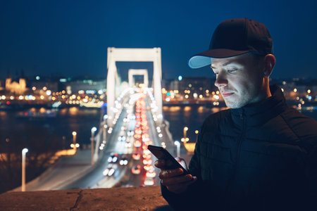 Young man in the city checking mobile phone on the street in the night. Budapest, Hungary.