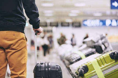 Man traveling by airplane. Young passenger holding his suitcase near baggage claim in airport terminal.の写真素材