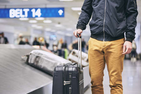 Man traveling by airplane. Young passenger holding his suitcase near baggage claim in airport terminal.の写真素材