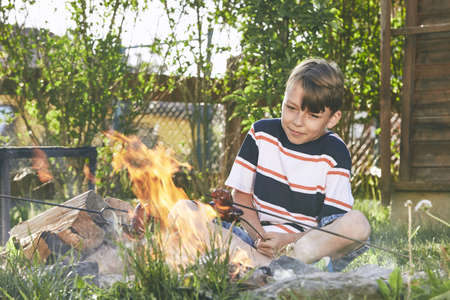 Children enjoy campfire. Boy toasting sausages on the garden.の写真素材