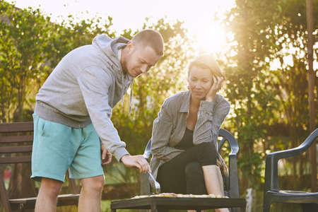 Summertime on the garden. Young couple barbecuing against chalet at the sunset.の写真素材
