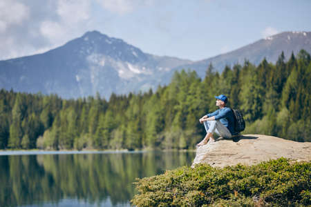 Young man (tourist) resting on rock above lake against mountain range of Alps. Pure nature in South Tyrol in Italy.の写真素材