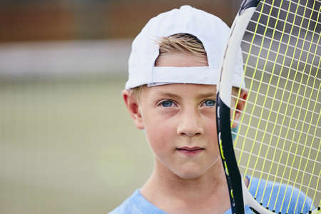 Little tennis player. Portrait of the little boy (6 years) holding tennis racket on the court.の写真素材