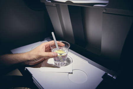Traveling by airplane. Passenger enjoying gin and tonic drink in economy class during flight.の写真素材