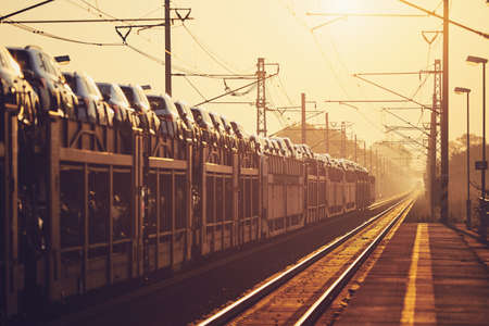Freight train with new cars commuting to railroad station at sunrise.の写真素材