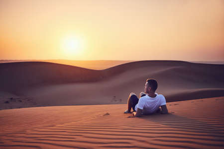 Idyllic sunrise in desert. Young man contemplation on sand dune. Wahiba Sands in Oman.の写真素材