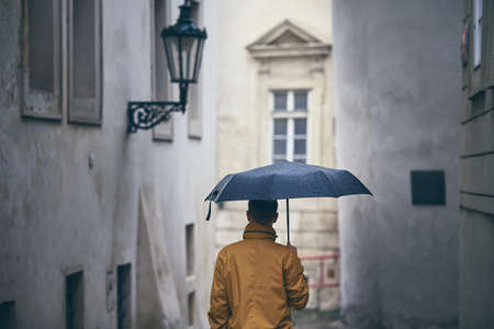 Man with umbrella walking in rain. Old city street in Prague, Czech Republicの写真素材