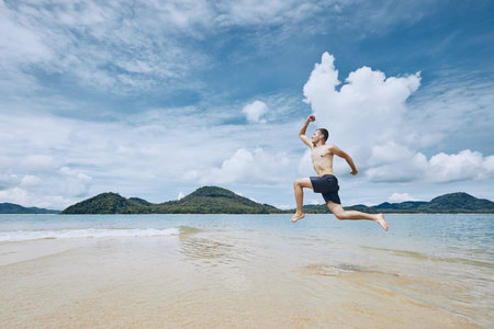 Happy young man jumping to the sea against tropical island.の写真素材
