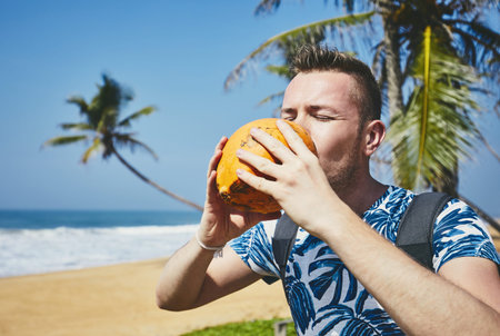 Thirsty young man drinking coconut water. Relaxation on the sand beach. Sri Lankaの写真素材