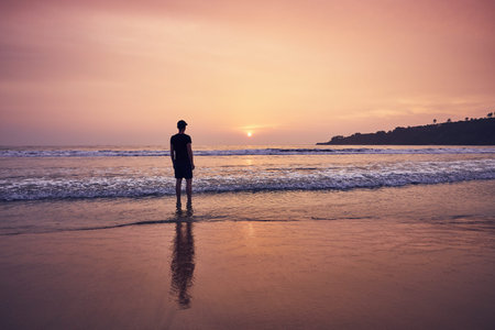 Contemplation during beautiful sunrise. Young man on idyllic sand beach near Tangalle in Sri Lanka.の写真素材