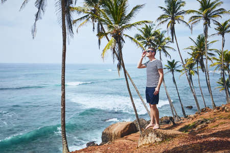 Young man with sunglasses relaxing under palm trees against sea. Coastline in Sri Lanka.の写真素材