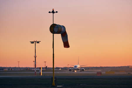 Striped windsock against taxiing airplane. Airport at sunset.の写真素材