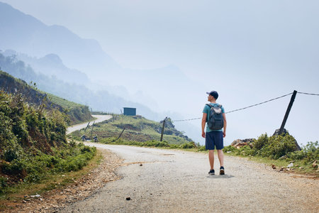 Man with backpack walking on winding road against foggy landscape. Sapa, Vietnam